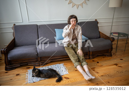 Exhausted indifferent woman lounging on sofa with cat resting nearby on floor in lethargy detachment 128535012