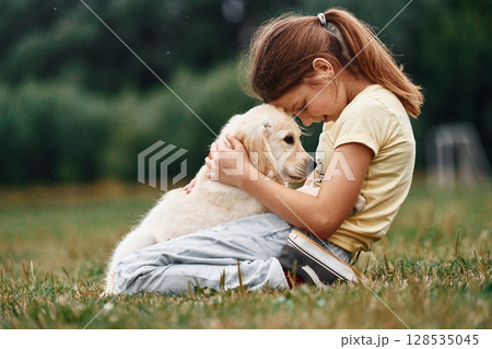 On the ground. Cute little girl is with golden retriever dog on the field On the ground. Cute little girl is with golden retriever dog on the field 128535045
