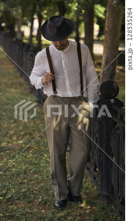 Man walking in vintage attire along park fence on sunny day 128535264