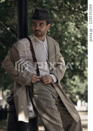 Man in vintage attire leaning casually against lamppost outdoors 128535269