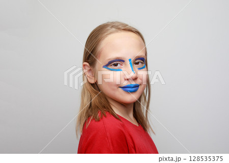 Happy girl child with vibrant blue and red face paint makeup on her cheeks and forehead Happy girl child with vibrant blue and red face paint makeup on her cheeks and forehead 128535375