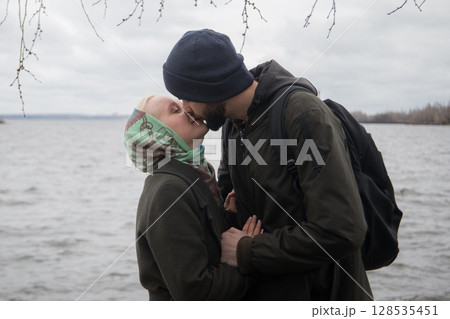 Portrait of man and young blond woman couple hugging each other kissing at seaside 128535451