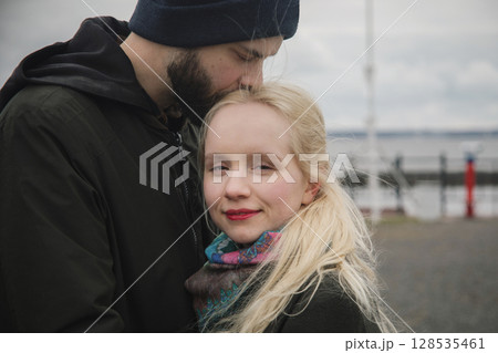 Beautiful young woman with long blonde hair and man couple hugging each other kissing at seaside Beautiful young woman with long blonde hair and man couple hugging each other kissing at seaside 128535461
