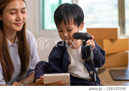 Sell Online: Young boy scanning items with mother in home office 128535536