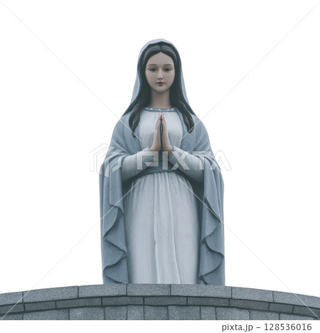 Serene statue of woman in blue and white robe stands with hands in prayer, symbolizing peace and devotion. figure is positioned on stone pedestal, evoking sense of reverence 128536016