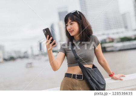 Happy young southeast asian woman teenager blogger world travel explorer using smartphone searching guide for local cultural experience. Tourism concept for Asia at Chao Phraya River Bangkok 128536635