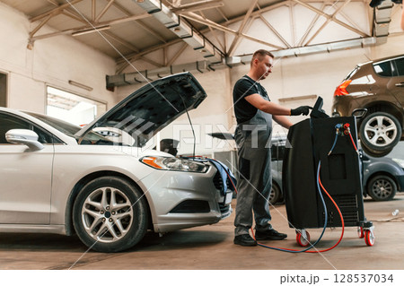 Using electric device. Man is works in the automobile repairing salon 128537034