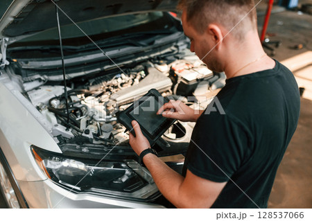 Holding the tablet. Man is works in the automobile repairing salon Holding the tablet. Man is works in the automobile repairing salon 128537066
