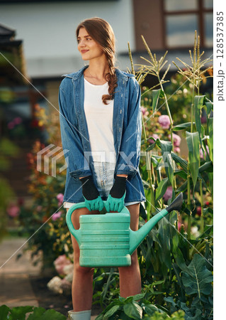 Standing and holding watering can. Beautiful young woman is gardening 128537385