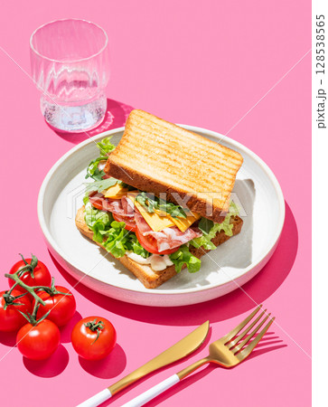 Toast bread sandwich with bacon, cheese, tomatoes, lettuce, arugula and sauce on a pink background Toast bread sandwich with bacon, cheese, tomatoes, lettuce, arugula and sauce on a pink background 128538565