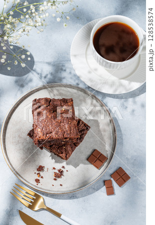 Chocolate brownie on a plate on a light background with cup of coffee, bouquet of flowers Chocolate brownie on a plate on a light background with cup of coffee, bouquet of flowers 128538574