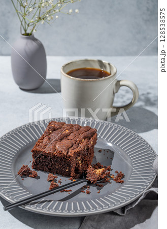 Chocolate brownie on a dark plate on a light background with cup of coffee, bouquet of flowers Chocolate brownie on a dark plate on a light background with cup of coffee, bouquet of flowers 128538575