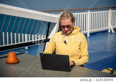 Woman working on laptop outdoors on ferry deck on sunny windy day 128538949