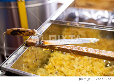 Electric knife for uncapping honey frames on the table. Harvest of honey on apiary, professional tool for opening honey frames, dirty in beeswax 128538972