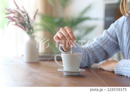 Casual woman hand at home stirring coffee on wooden table Casual woman hand at home stirring coffee on wooden table 128539375