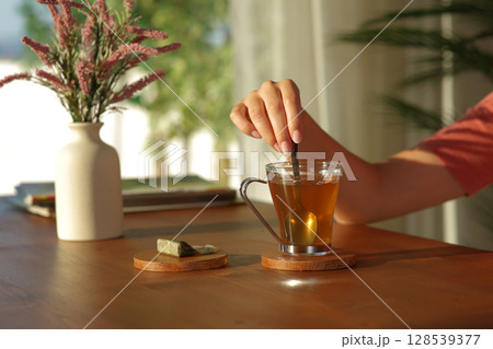 Woman hand stirring tea in a glass at sunset at home 128539377
