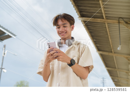 Young non binary tourist traveler in train station using phone Young non binary tourist traveler in train station using phone 128539581