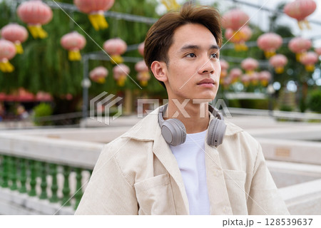 Asian non binary tourist person with headphones relaxing at park near lake 128539637
