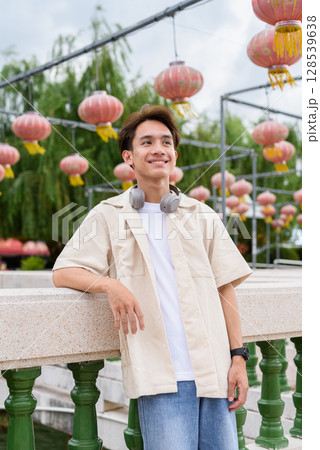 Asian non binary tourist person with headphones relaxing at park near lake Asian non binary tourist person with headphones relaxing at park near lake 128539638