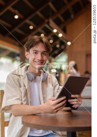 Handsome young non binary man sitting in cafe restaurant using digital tablet computer Handsome young non binary man sitting in cafe restaurant using digital tablet computer 128539655