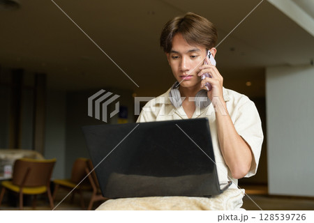 Non binary Asian student man sitting in modern coffee shop using laptop computer Non binary Asian student man sitting in modern coffee shop using laptop computer 128539726