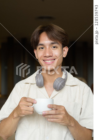 Non binary Asian student man sitting in modern cafe drinking coffee 128539743