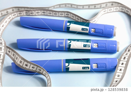 Three Ozempic syringe drug pen and measuring tape on blue 128539838