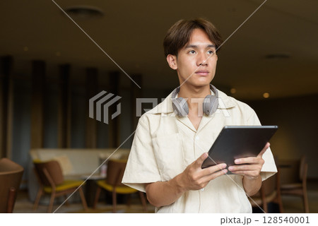 Non binary Asian student man sitting in modern coffee shop using digital tablet computer Non binary Asian student man sitting in modern coffee shop using digital tablet computer 128540001