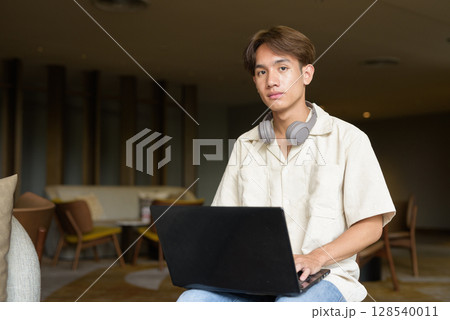 Non binary Asian student man sitting in modern coffee shop using laptop computer 128540011