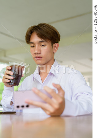 Non binary university student sitting in college campus using phone Non binary university student sitting in college campus using phone 128540046