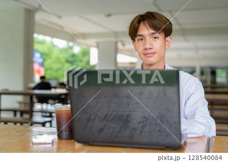 Non binary university student sitting in college campus using laptop computer 128540084