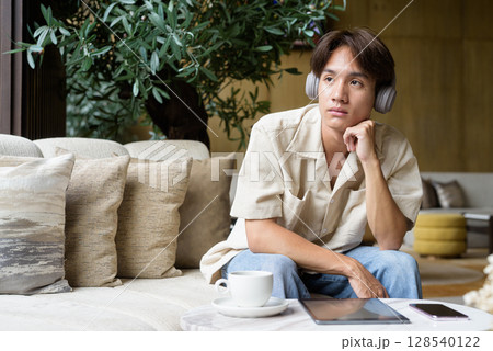 Non binary Asian student man sitting in modern coffee shop wearing headphones Non binary Asian student man sitting in modern coffee shop wearing headphones 128540122