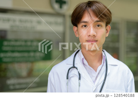 Young healthcare worker wearing lab coat in front of medical clinic Young healthcare worker wearing lab coat in front of medical clinic 128540188