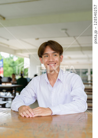 Non binary university student sitting and smiling in college campus Non binary university student sitting and smiling in college campus 128540257