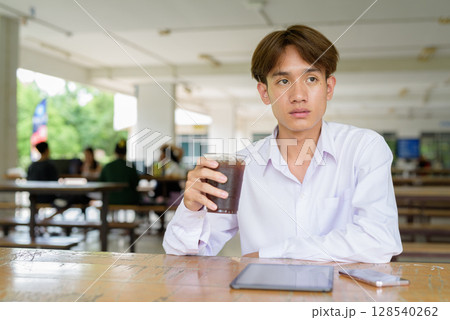 Non binary university student sitting in college campus 128540262