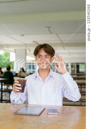 Non binary university student sitting in college campus using phone Non binary university student sitting in college campus using phone 128540268