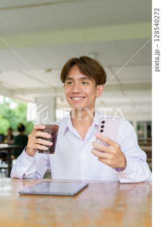 Non binary university student sitting in college campus using phone 128540272