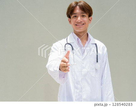 Young healthcare worker wearing lab coat giving handshake Young healthcare worker wearing lab coat giving handshake 128540283