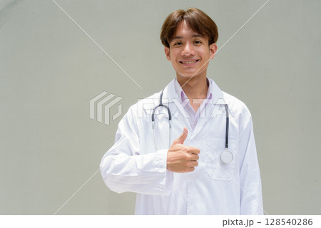 Young healthcare worker wearing lab coat giving thumbs up Young healthcare worker wearing lab coat giving thumbs up 128540286