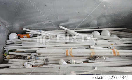 Discarded light bulbs and tubes in a metal container at a recycling center during midday operations 128541445
