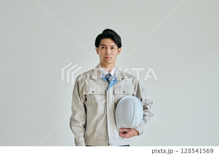 ヘルメットを持つ作業服姿の若い男性 ヘルメットを持つ作業服姿の若い男性 128541569