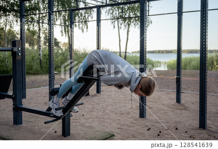 Young woman doing exercise at outdoor gym near lake in summer 128541639