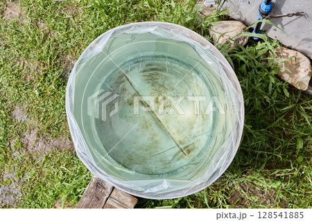 Inserting rain barrel liner into water barrel positioned on garden lawn, top view captured with wide angle showing filled container interior. 128541885