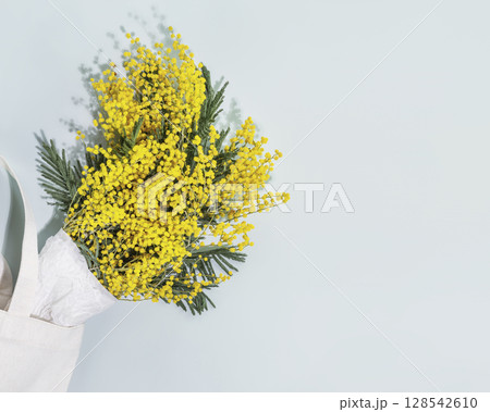 Bouquet with mimosa branches on blue background. Eco friendly still life with mimosa flowers in textile bag. Floristic spring background suitable for mothers day or womans day. Flat lay, copy space Bouquet with mimosa branches on blue background. Eco friendly still life with mimosa flowers in textile bag. Floristic spring background suitable for mothers day or womans day. Flat lay, copy space 128542610