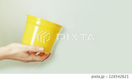 Greenery home and Home gardening concept. Spring composition with female hand holding empty yellow garden pot on blue background with copy space. Hobby and relax 128542621