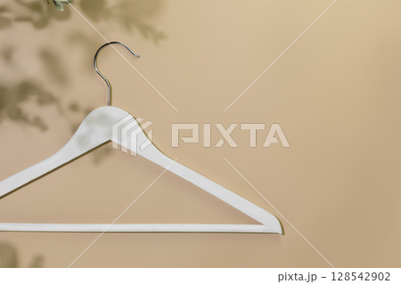 Sustainable shopping, buying or sales concept. Eco friendly still life with white wooden hanger on beige background with plant shadows. Flat lay, copy space Sustainable shopping, buying or sales concept. Eco friendly still life with white wooden hanger on beige background with plant shadows. Flat lay, copy space 128542902
