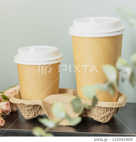 Spring romantic eco friendly card with two disposable cardboard cups with coffee on wooden table on blue background with eucalyptus branch. Dating or love concept. Coffee to go. Morning still life Spring romantic eco friendly card with two disposable cardboard cups with coffee on wooden table on blue background with eucalyptus branch. Dating or love concept. Coffee to go. Morning still life 128542909