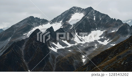 A rugged mountain range with jagged, rocky peaks partially covered in snow. 128543202