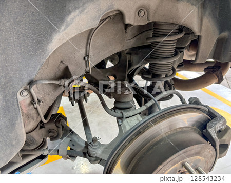 An intricate view of a vehicle's suspension system show various component like shock absorber and brake system in an auto repair facility during daylight hour. 128543234