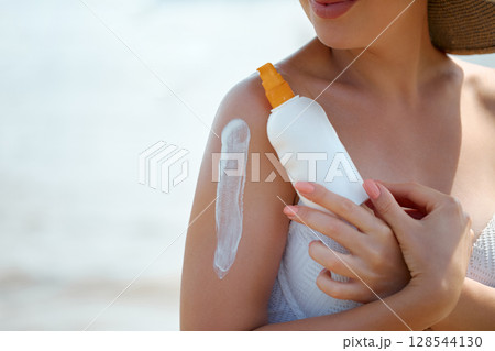 Woman Applying Sunscreen at Beach to Protect Skin From Sunlight 128544130